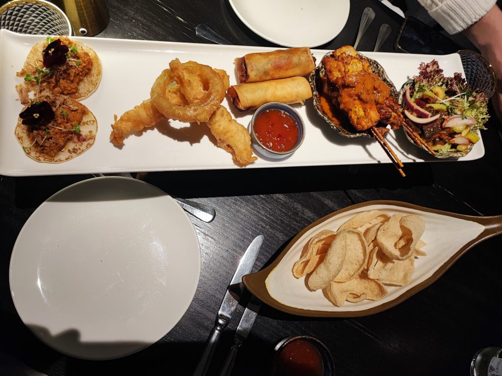 Platter of Thai Chicken tacos, tempura prawns, spring rolls, chicken satay skewers and a duck salad. A bowl of prawn crackers.